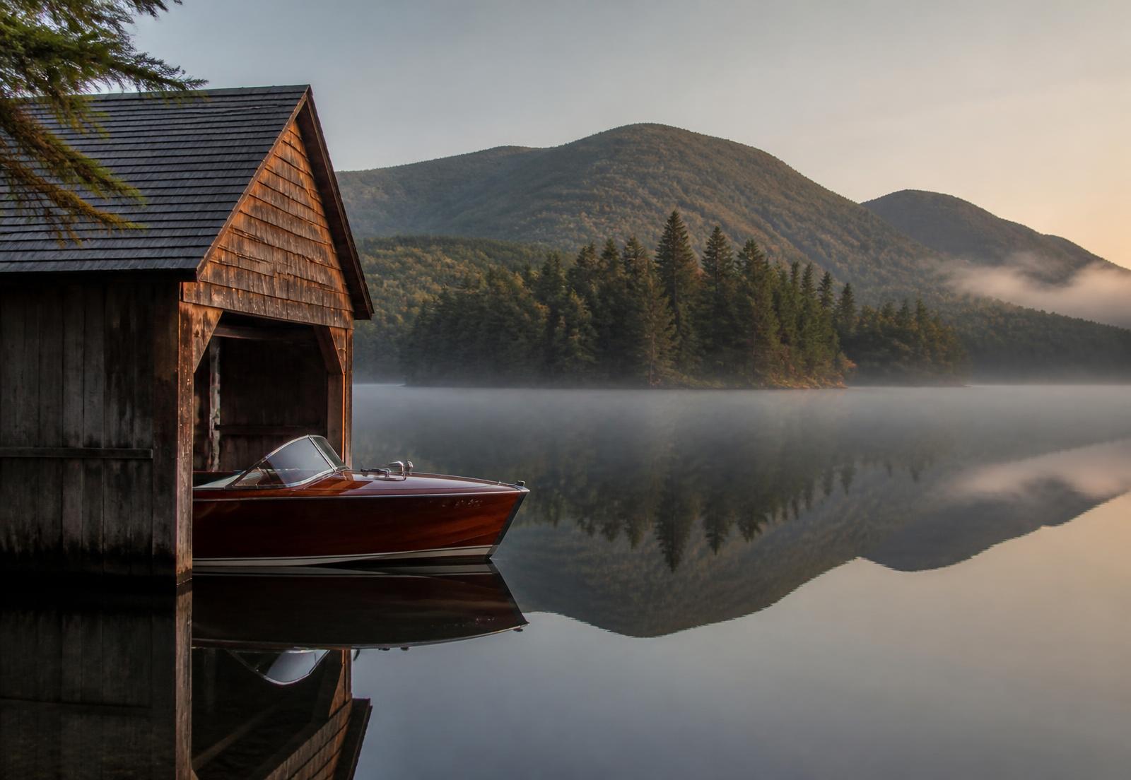 Adirondack boathouse and classic wooden boat on a still lake at dawn